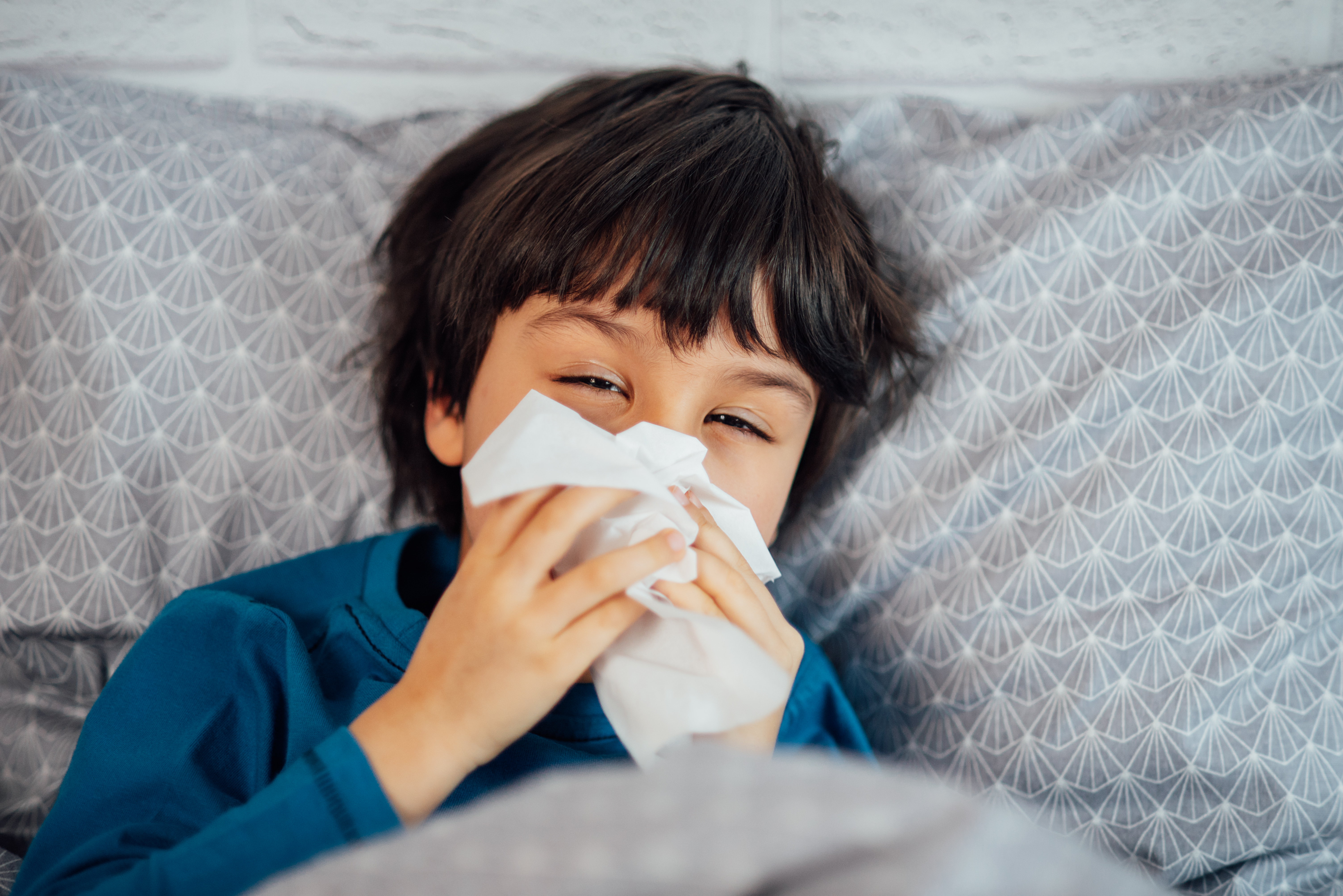 Little child boy blowing his nose. Sick child with napkin in bed